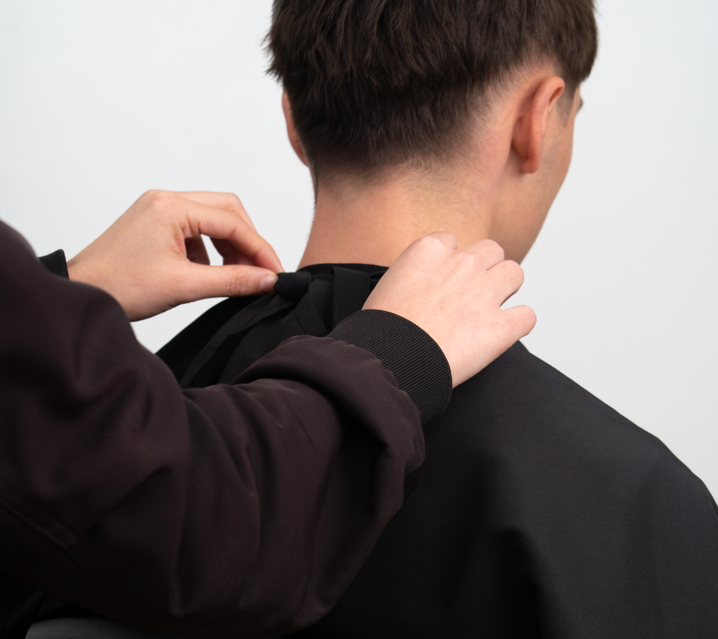 Preparación para corte de cabello: manos atando capa de peluquería en cliente masculino - Luxent Professional