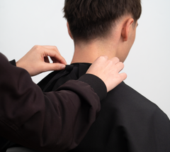 Preparación para corte de cabello: manos atando capa de peluquería en cliente masculino - Luxent Professional
