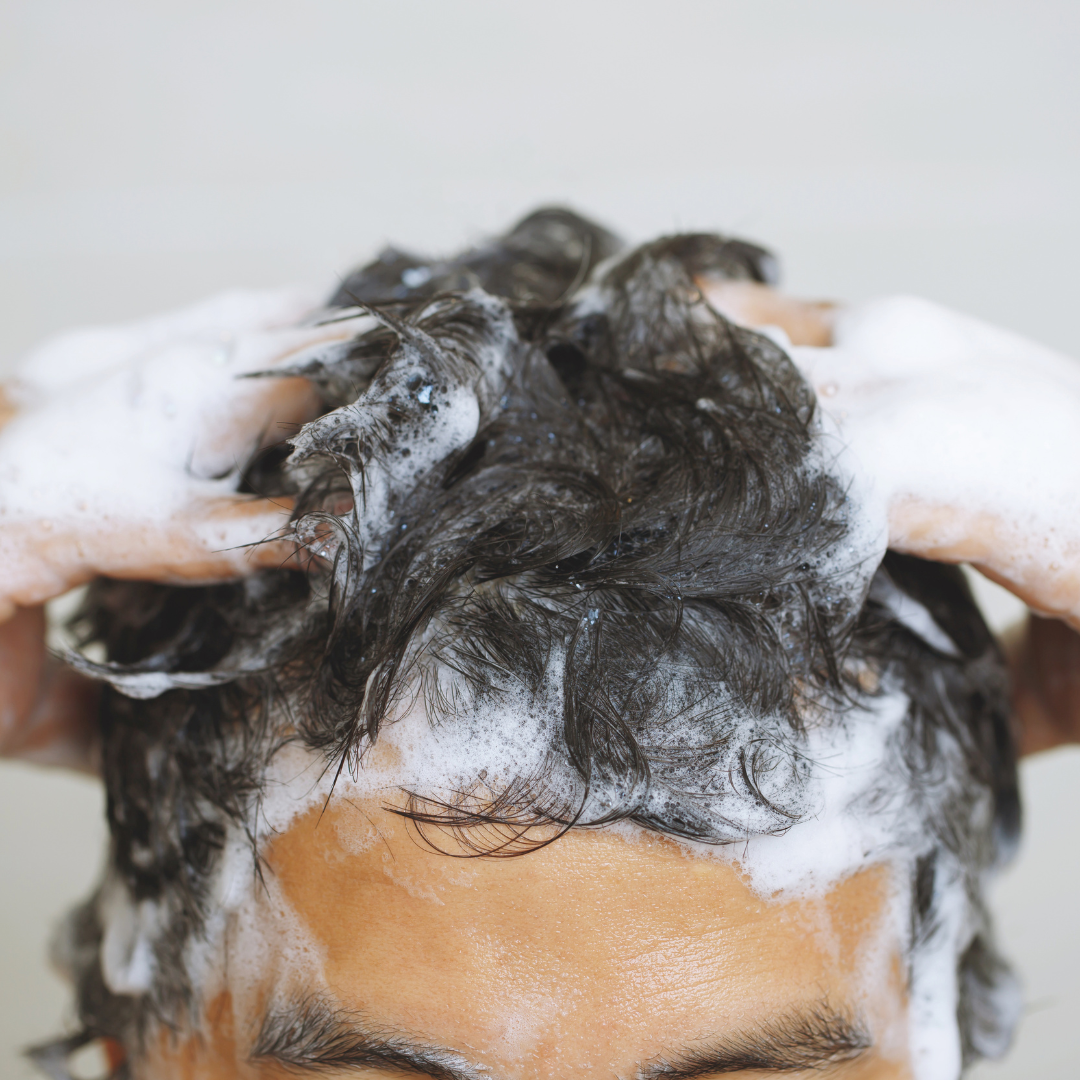 Persona lavando su cabello oscuro con champú, creando mucha espuma. Cuidado capilar profesion - Luxent Professional