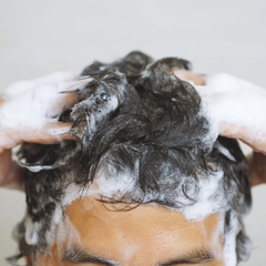 Persona lavando su cabello oscuro con champú, creando mucha espuma. Cuidado capilar profesion | L'xent Professional