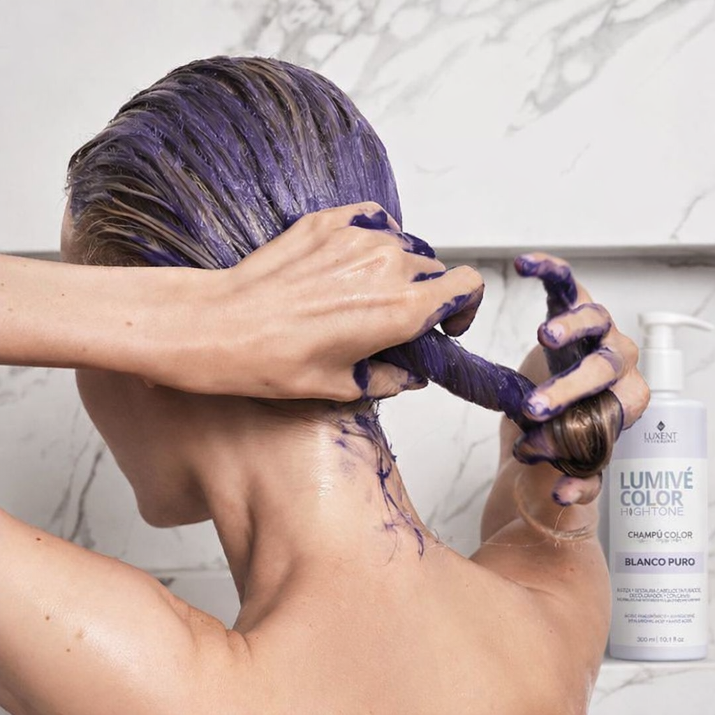 Mujer aplicando champú violeta matizador en cabello rubio, con botella de Luxent Lumivé Color - Luxent Professional