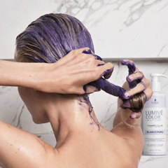 Mujer aplicando champú violeta matizador en cabello rubio, con botella de Luxent Lumivé Color - Luxent Professional