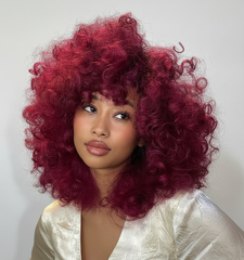 Modelo con cabello rizado voluminoso color rojo magenta vibrante, ideal para tintes profesion - Luxent Professional